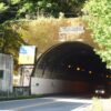 看板が立つ山あいのトンネル出口へ続く道路