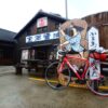 「金両醤油」の建物前に停めた赤いロードバイクと樽の看板