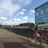 河川標識「鶴見川」の前に停めた赤いロードバイクと土手沿いの遊歩道