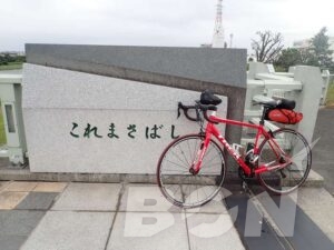 「これまさばし」と刻まれた石碑の前に停めた赤いロードバイク