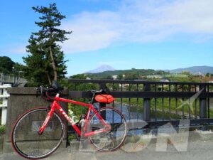 松の木と橋の欄干越しに見える富士山と赤いロードバイク