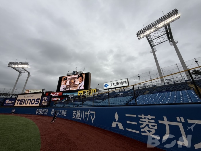 神宮球場の照明塔とスコアボードを外野フェンス際から見上げた様子