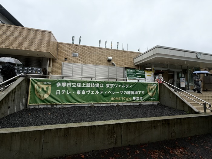 「多摩市立陸上競技場は東京ヴェルディ・日テレ東京ヴェルディベレーザの練習場です」と書かれた緑色の横断幕