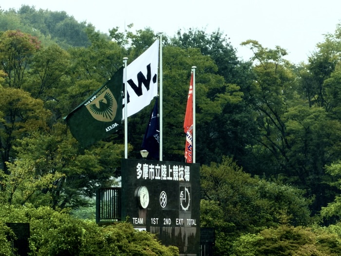 「多摩市立陸上競技場」と書かれたスコアボードとベレーザのクラブフラッグ